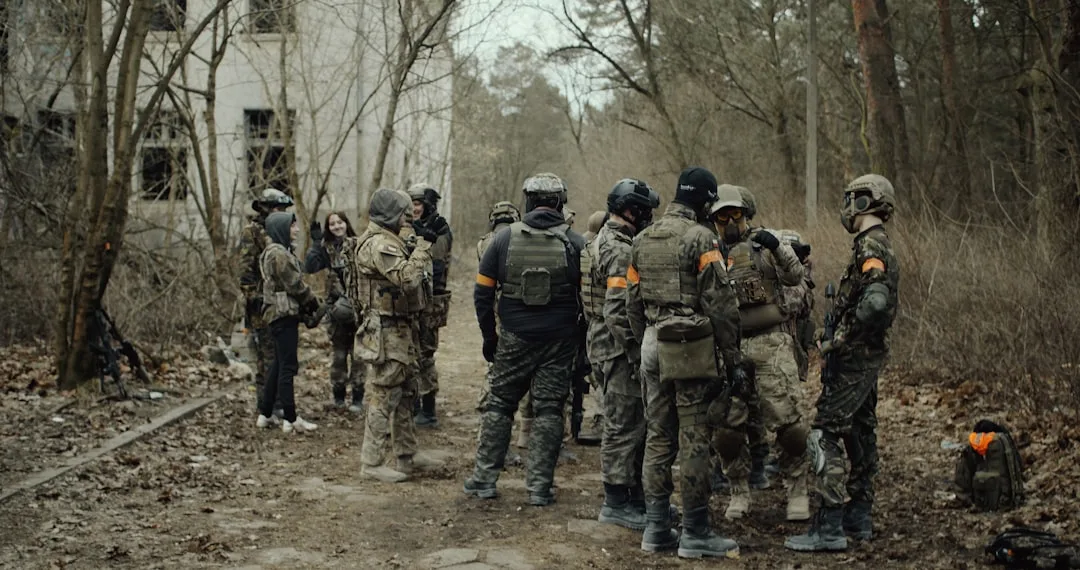 Un groupe de collègues en équipement de paintball écoutent les consignes d'un instructeur en extérieur.
