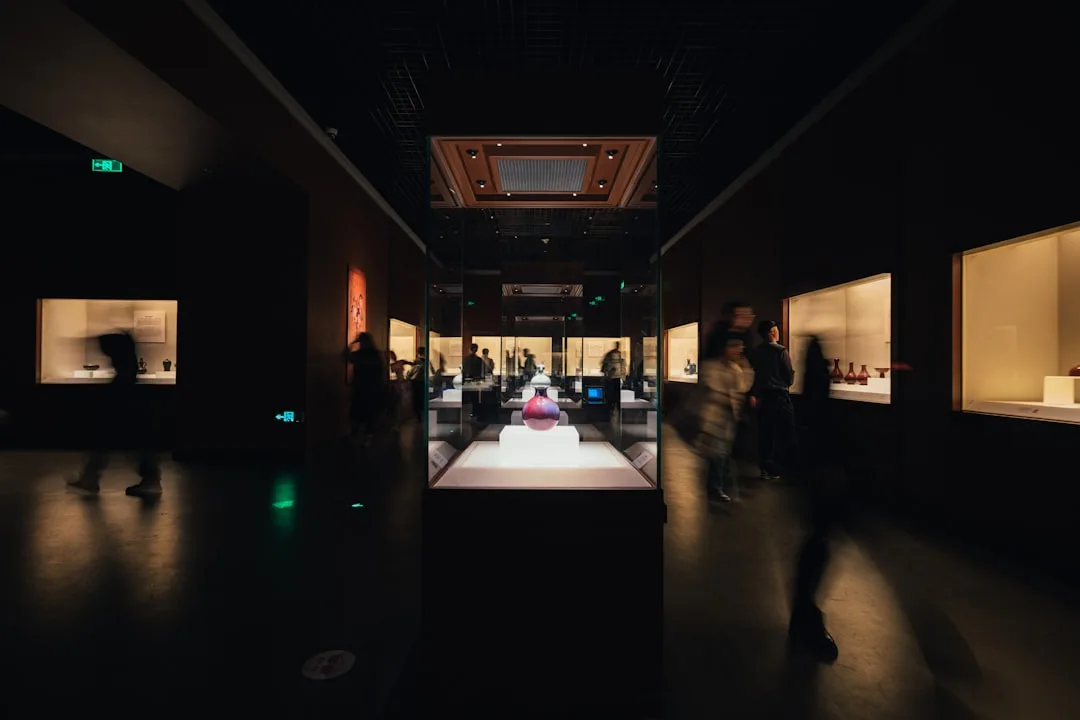 Visiteurs parcourant une exposition muséale moderne avec éclairage sophistiqué et scénographie soignée